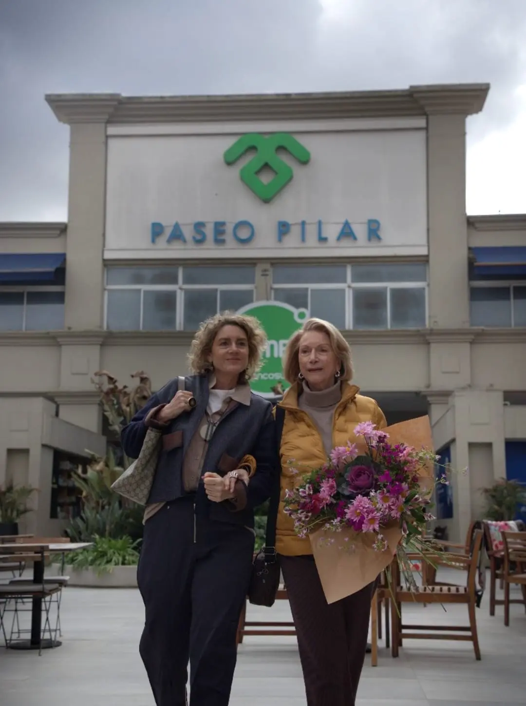 Dos mujeres con flores frente al cartel de Paseo Pilar